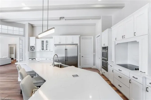 a large kitchen with white cabinets a sink dishwasher a dining table chairs and wooden floor