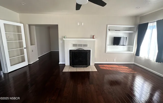 a view of an empty room with wooden floor fireplace and a window