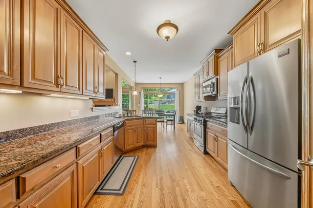 a kitchen with granite countertop a refrigerator a sink dishwasher and wooden cabinets with wooden floor
