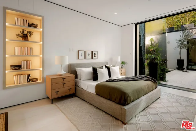 a spacious bedroom with a bed a table and large mirror with wooden floor
