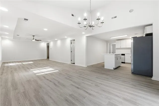 a view of an empty room with wooden floor and kitchen view