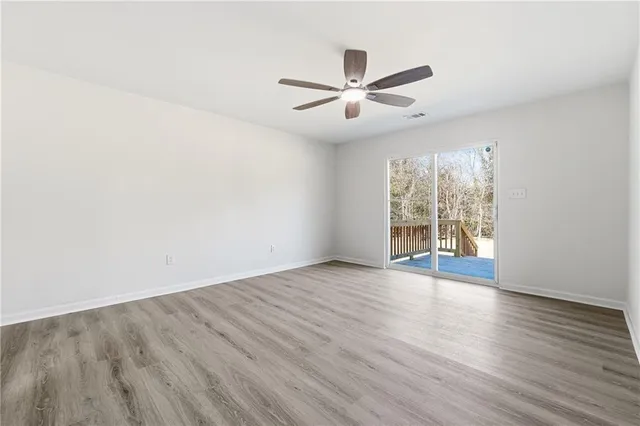 an empty room with wooden floor fan and windows