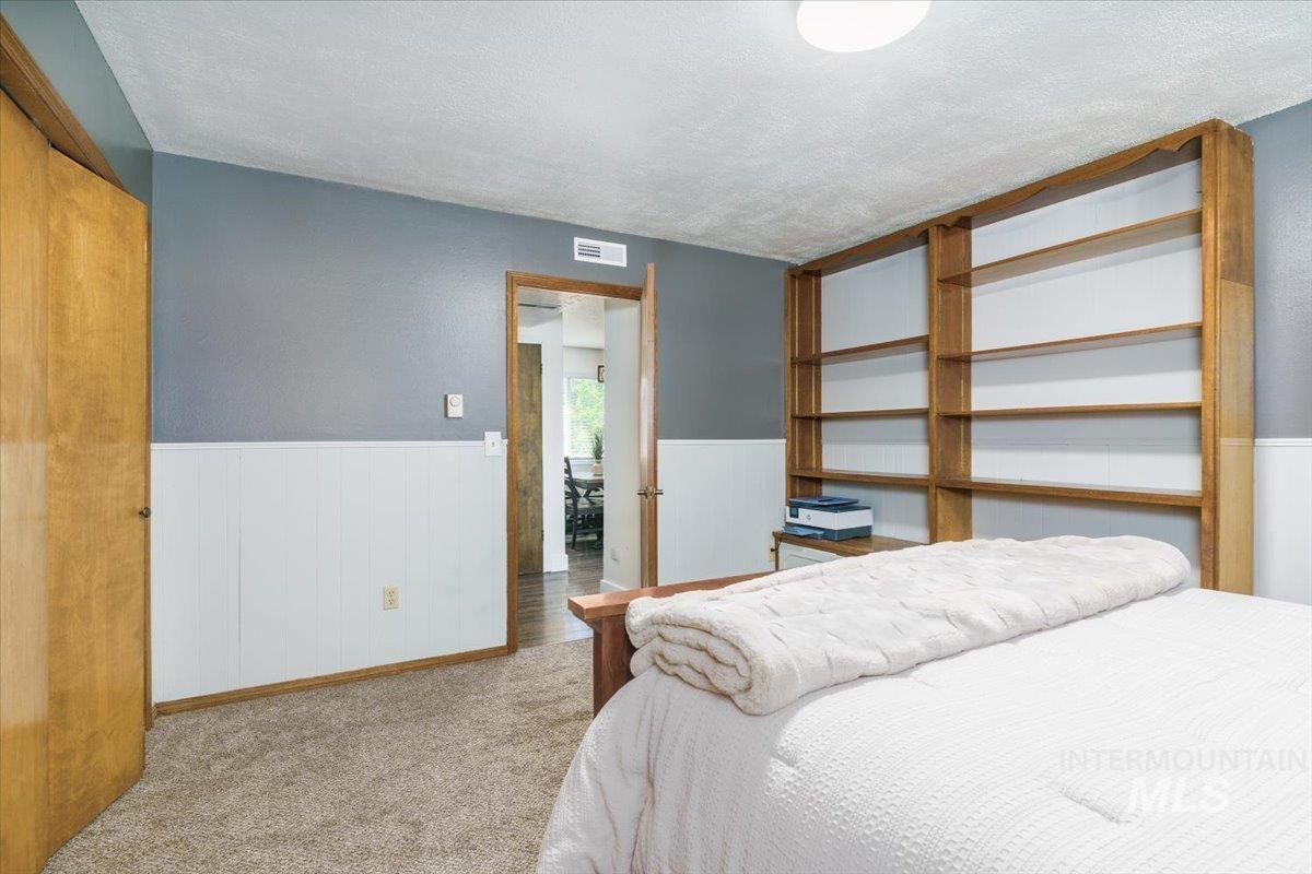 1401 Chokecherry Drive Pocatello, ID 83204 - Photo 22 of 46 Room featuring built-in wooden shelving, neutral carpet flooring, and two-tone wall treatment with a white wainscoting panel
