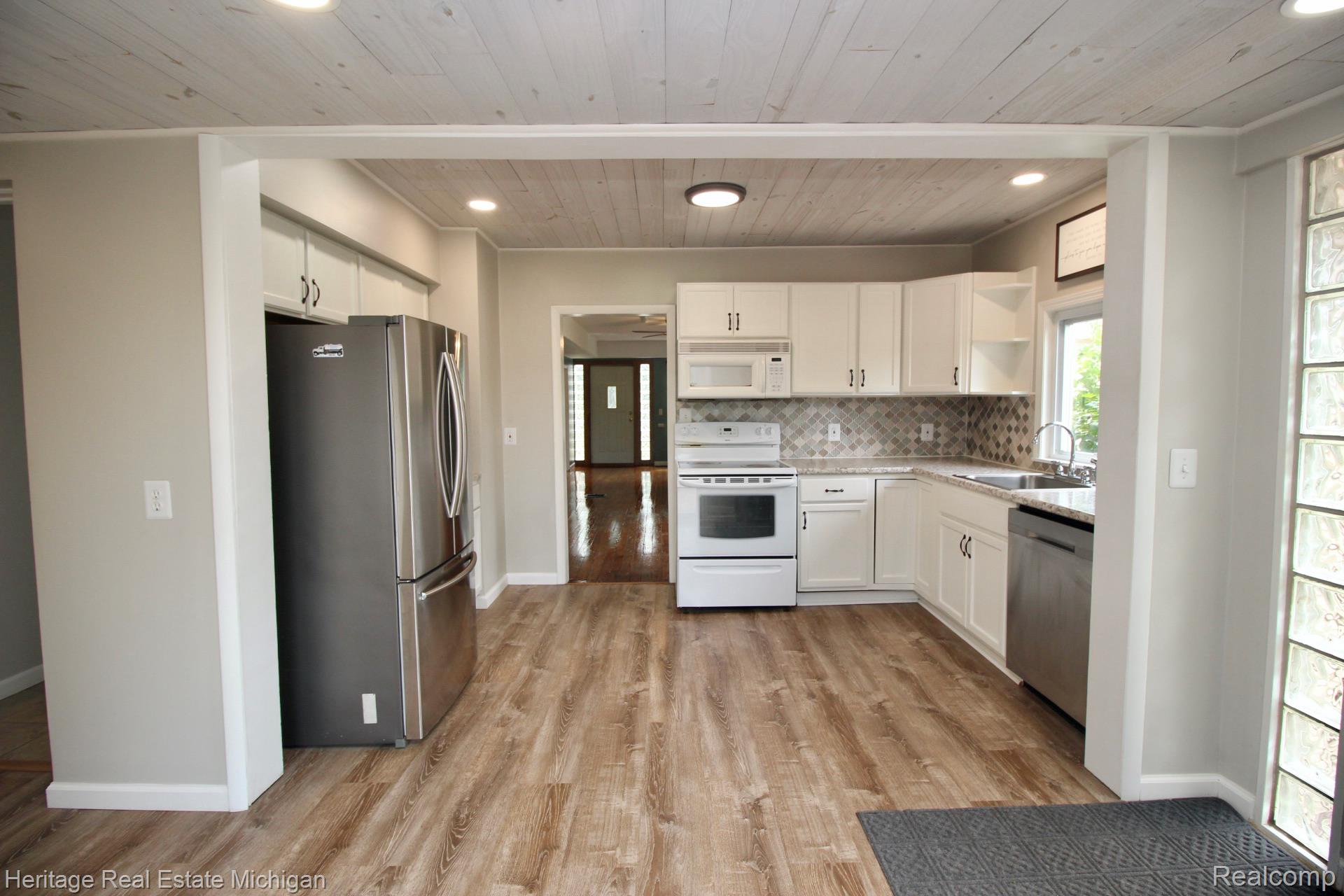 15352 South Duffield Road Byron, MI 48418 - Photo 5 of 47 Well-appointed kitchen featuring white cabinetry, a mosaic tile backsplash, stainless steel dishwasher, and wood-finish flooring