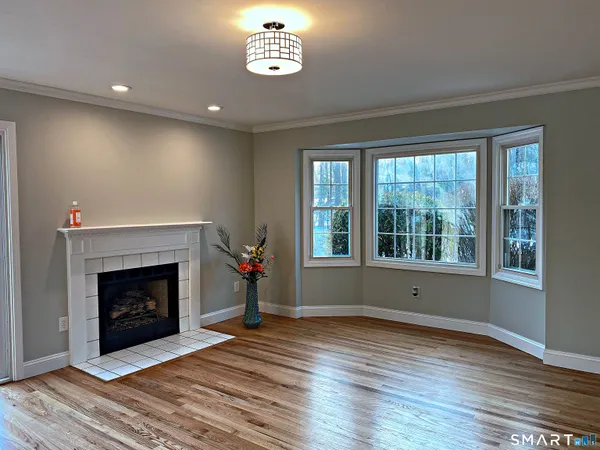a view of an empty room with wooden floor fireplace and a window
