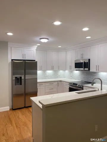 a kitchen with stainless steel appliances granite countertop a sink a stove a refrigerator a oven and white cabinets