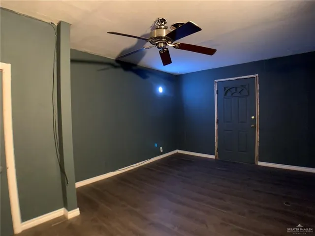 a view of an empty room with wooden floor and a ceiling fan