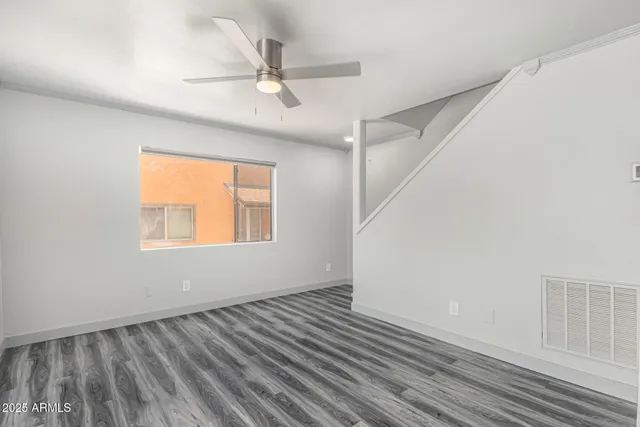 an empty room with wooden floor fan and windows