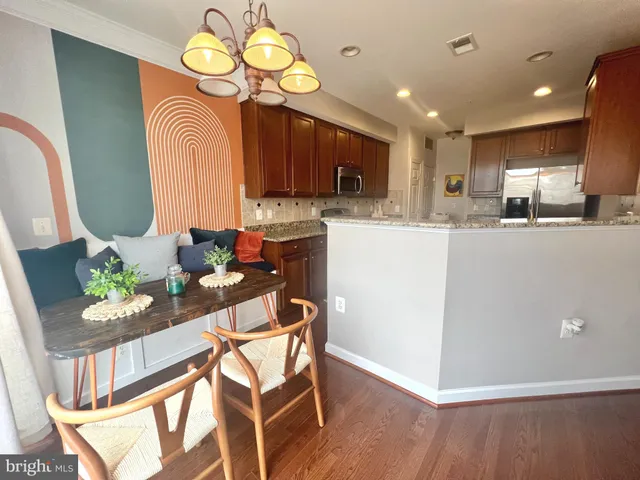 a kitchen with stainless steel appliances kitchen island granite countertop a refrigerator a stove a microwave oven a dining table and chairs with wooden floor