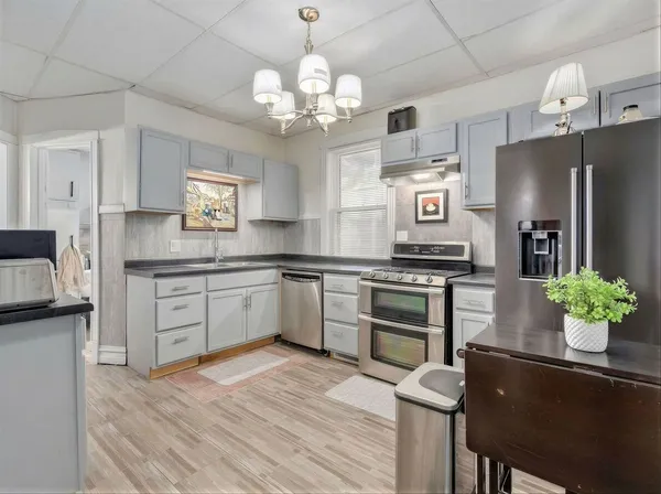 a kitchen with stainless steel appliances kitchen island granite countertop a refrigerator a sink dishwasher a stove and white cabinets with wooden floor