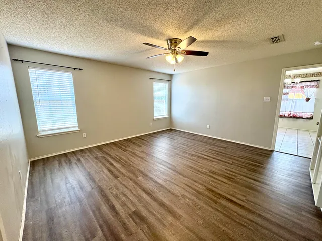 an empty room with wooden floor fan and windows