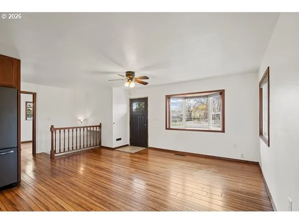 a view of an empty room with wooden floor and a ceiling fan