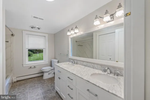 a bathroom with a granite countertop double vanity sink a mirror and a toilet
