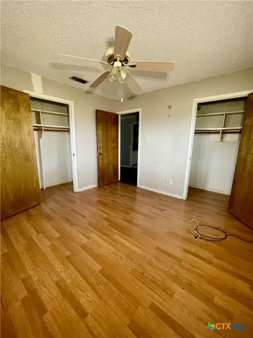 a view of an empty room with wooden floor and a ceiling fan