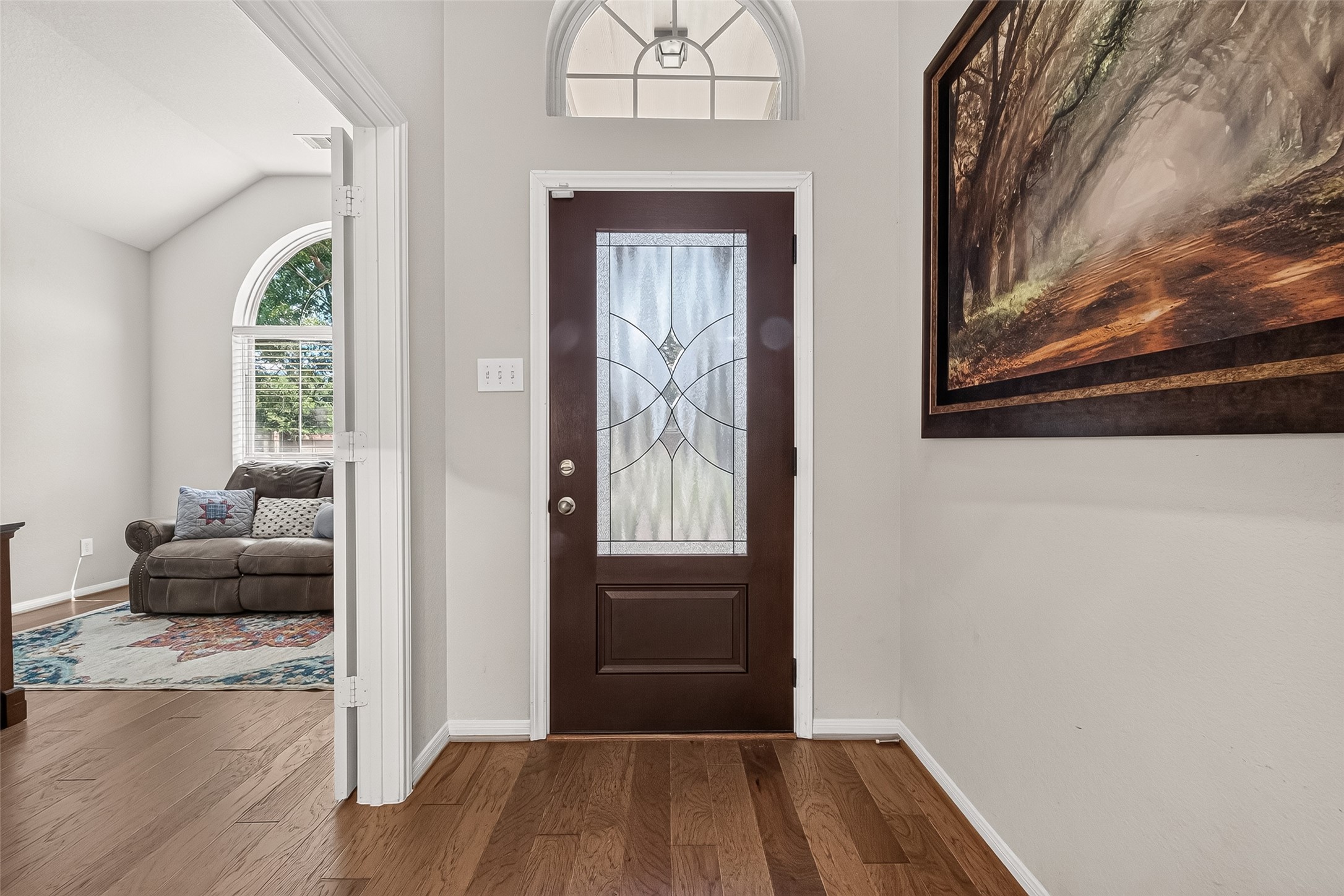 4910 Culver Lane Rosenberg, TX 77471 - Photo 8 of 50 The photo showcases a welcoming entryway with a LEADED GLASS SOLID WOOD front door, hardwood flooring, and large framed wall art. To the left, an open, double doorway leads to YOUR HOME OFFICE/STUDY featuring a large window with plentiful natural light.