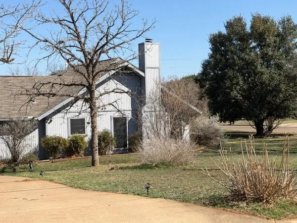 a view of a white house next to a yard with big trees