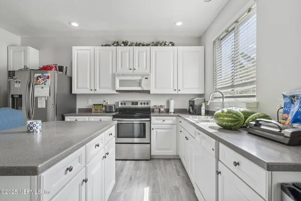 a kitchen with stainless steel appliances white cabinets a sink a stove a refrigerator and white cabinets