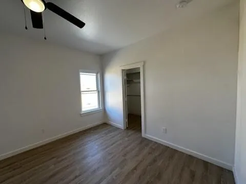 an empty room with wooden floor fan and windows