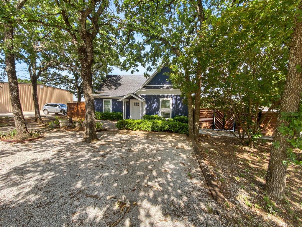 815 Stonecrest Road Argyle, TX 76226 - Photo 11 of 17 Deep blue exterior with white trim, covered front entry, gravel driveway, mature trees, and privacy fencing