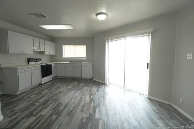 a kitchen with granite countertop a stove a sink and white cabinets with wooden floor