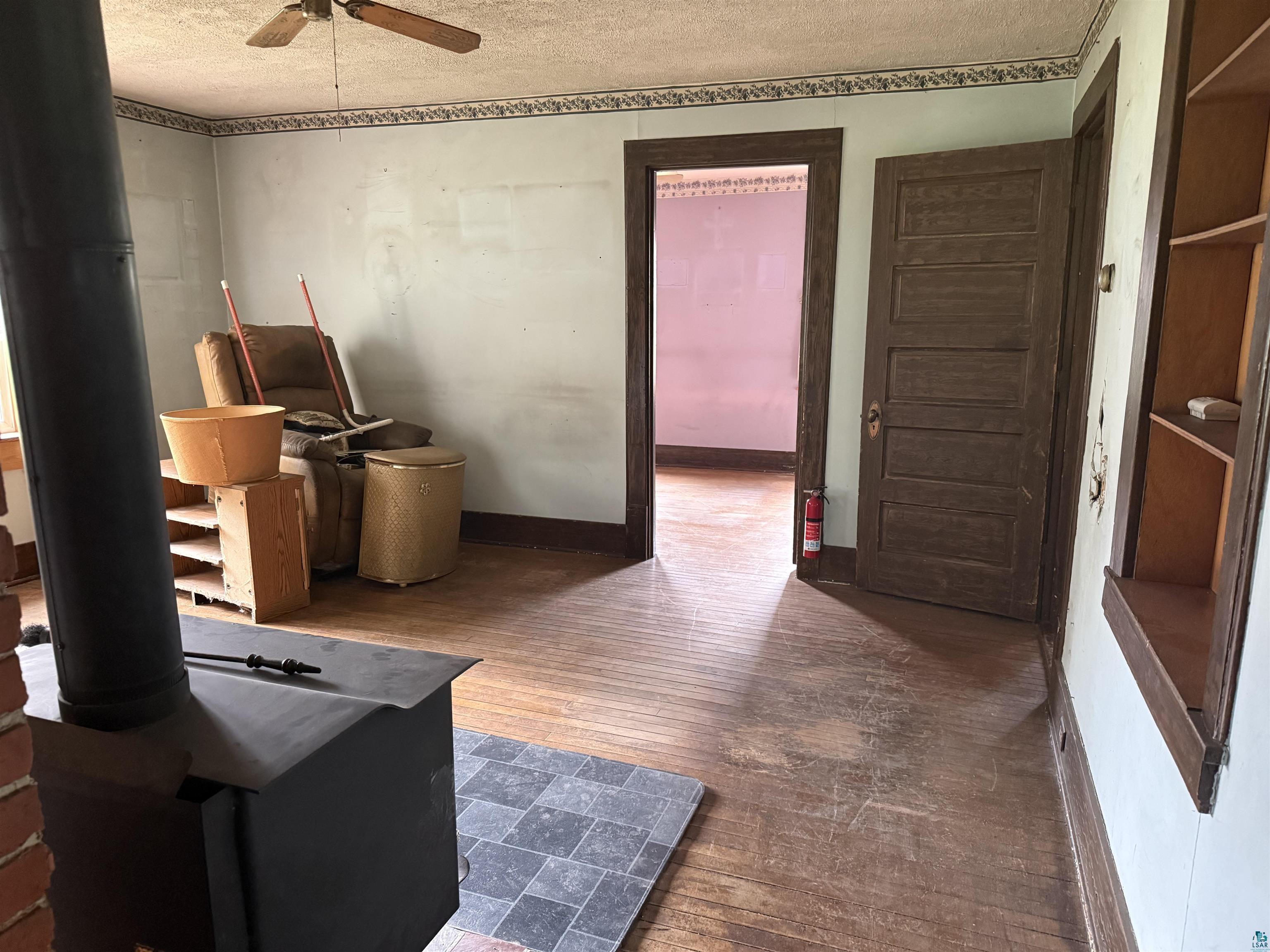 3541 Bent Trout Lake Road Barnum, MN 55707 - Photo 15 of 41 Room with wood-finish flooring, a wood-burning stove with a brick surround, and a ceiling fan