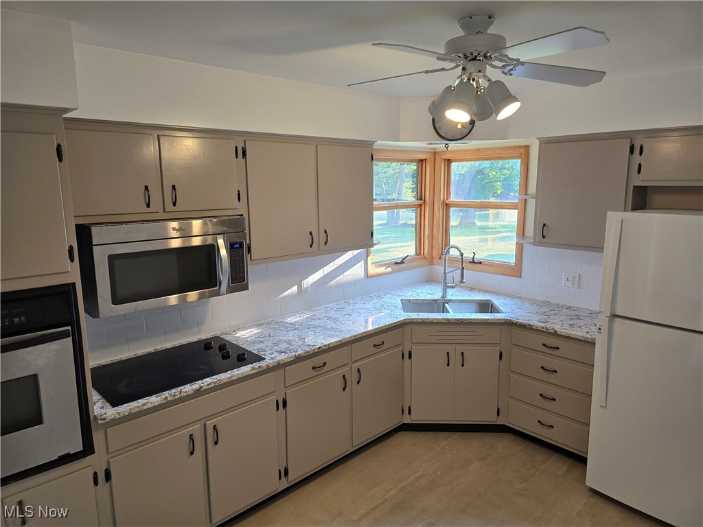 67 Moore Road Akron, OH 44319 - Photo 4 of 15 Kitchen featuring stainless steel appliances, sink, decorative backsplash, ceiling fan, and light stone counters