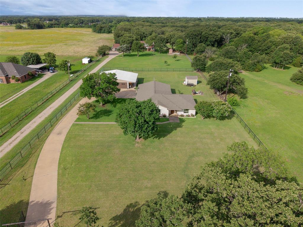 380 Farr Altom Road Seagoville, TX 75159 - Photo 25 of 30 Expansive property featuring a curved concrete driveway, a single-story residence with a gabled roof, an auxiliary structure with an open-sided portion, mature trees, and perimeter fencing