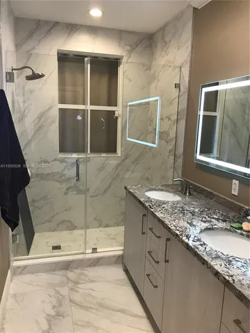 a bathroom with a granite countertop sink a mirror and shower