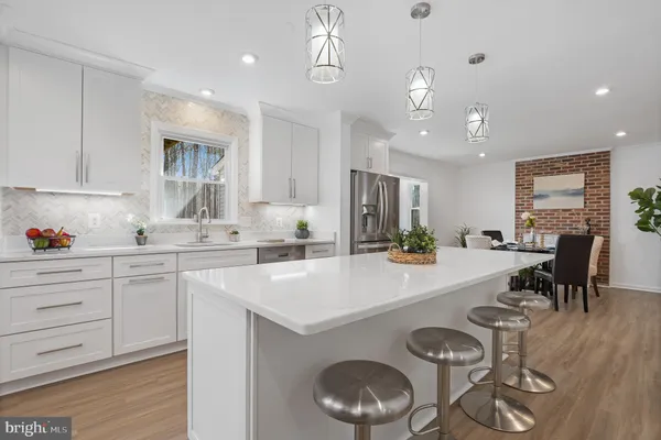 a kitchen with stainless steel appliances kitchen island granite countertop a refrigerator a stove a sink and white cabinets with wooden floor