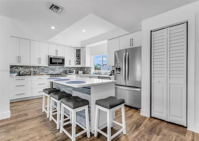 a kitchen with stainless steel appliances kitchen island granite countertop a dining table chairs and refrigerator