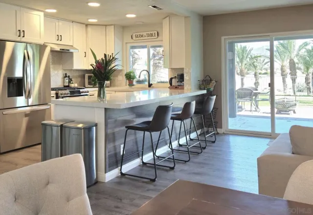 a kitchen with stainless steel appliances granite countertop a refrigerator a sink dishwasher a dining table and chairs with wooden floor