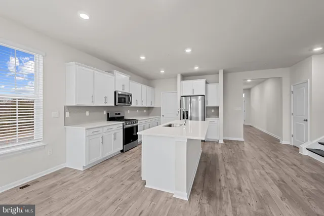 a large white kitchen with kitchen island a stove a sink dishwasher a refrigerator and white cabinets with wooden floor