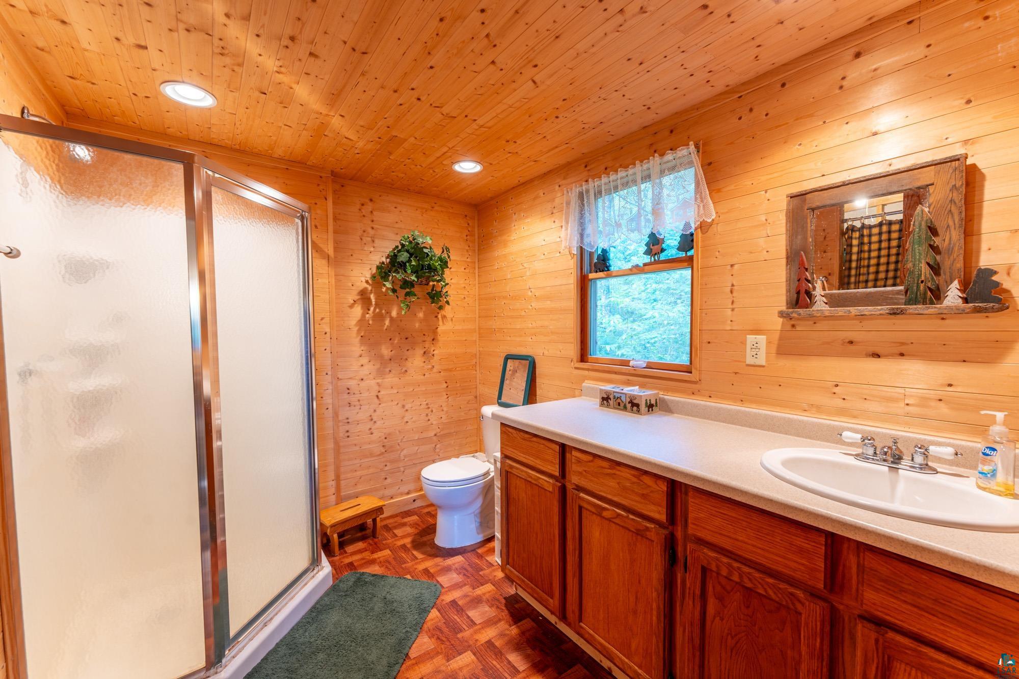 296 Shady Lane Ely, MN 55731 - Photo 14 of 27 Bathroom with wooden walls, parquet flooring, toilet, wood ceiling, and vanity