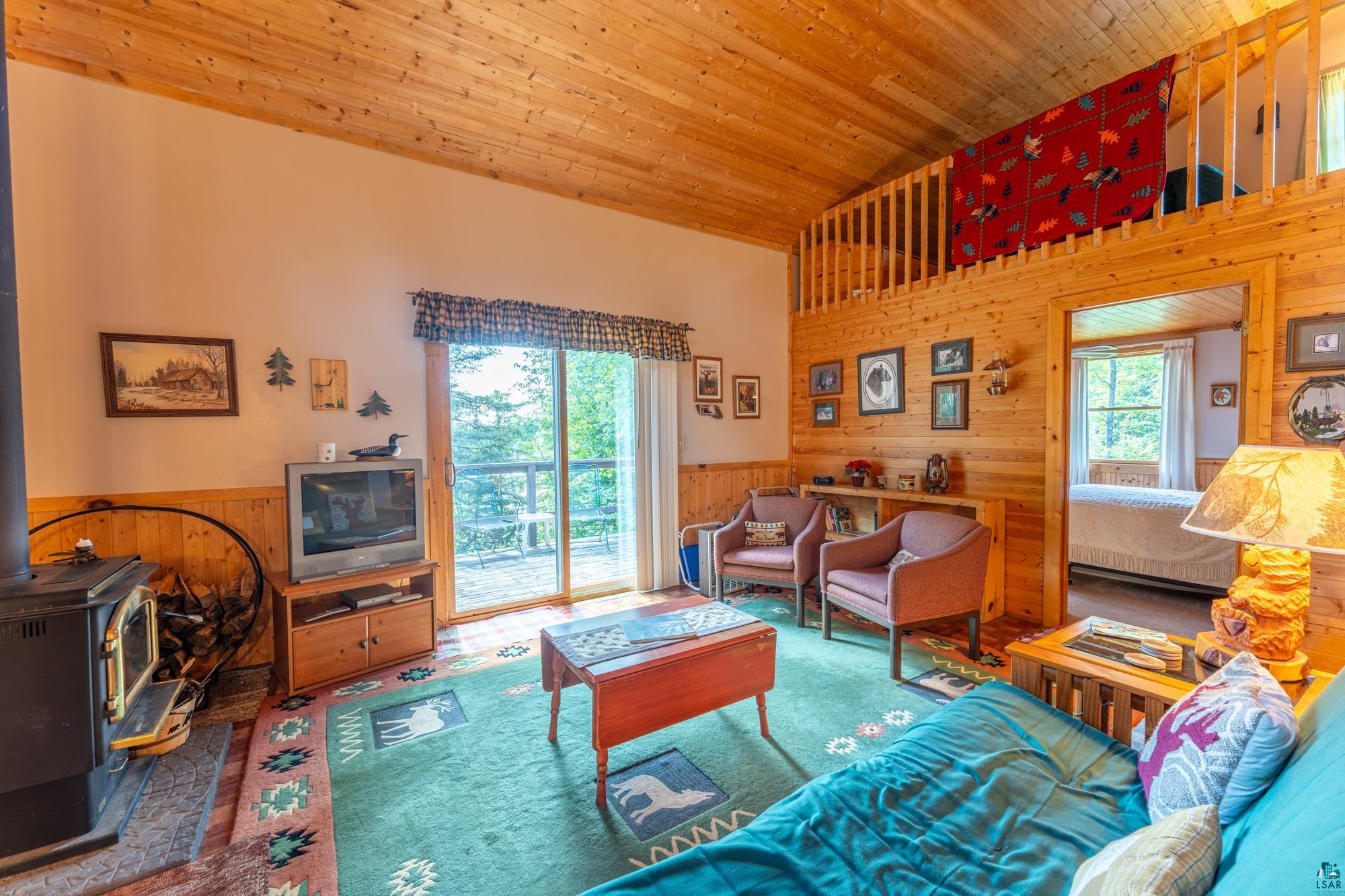 296 Shady Lane Ely, MN 55731 - Photo 9 of 27 Living room with wood ceiling, a high ceiling, wooden walls, and a wood stove