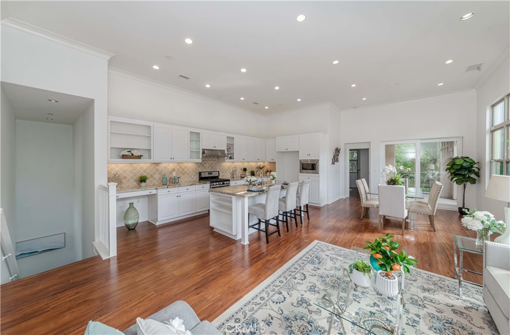 a living room with stainless steel appliances furniture wooden floor and a kitchen view