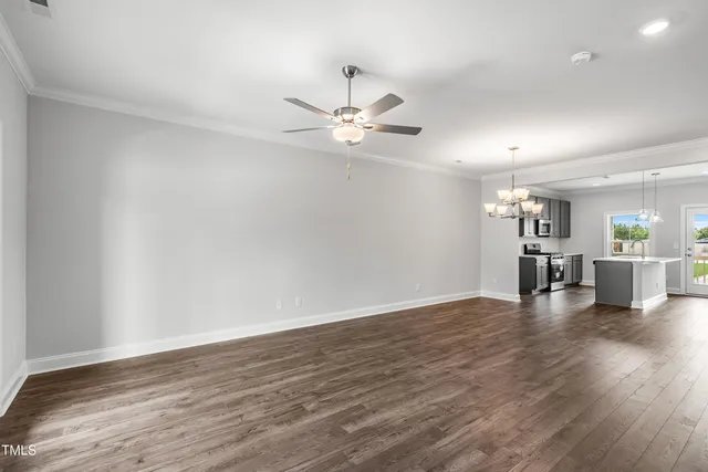 a view of an empty room and kitchen with hardwood floor