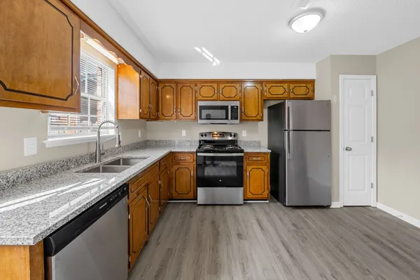 a kitchen with a sink a refrigerator a stove top oven a wooden floor and a window