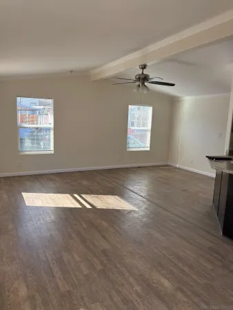 an empty room with wooden floor chandelier fan and windows