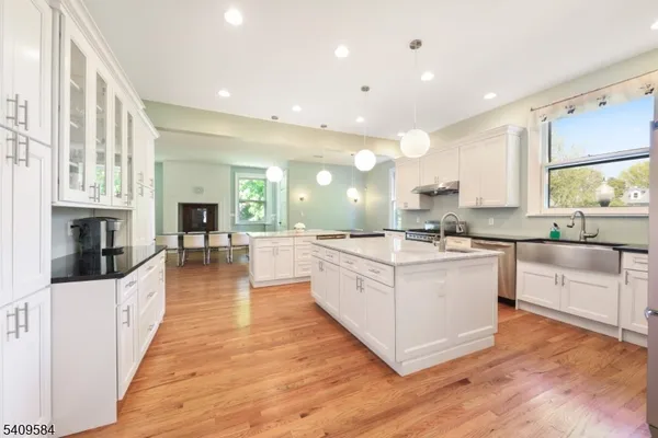 a large white kitchen with a large counter top a sink a window and stainless steel appliances