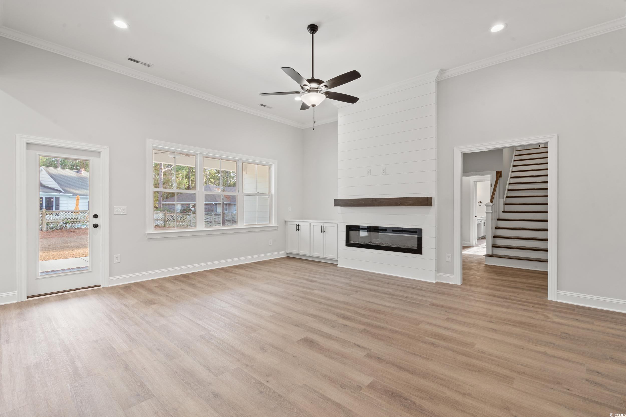 118 Goodson Loop Pawleys Island, SC 29585 - Photo 3 of 22 Unfurnished living room featuring a ceiling fan, a fireplace, light wood finished floors, stairs, and crown molding