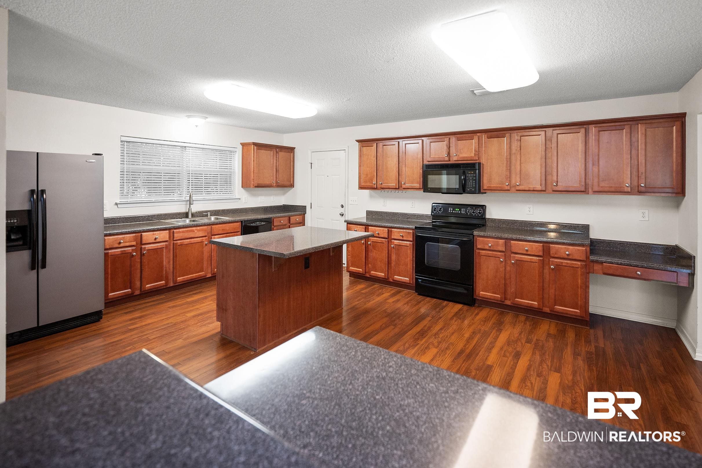 323 Manchester Lane Foley, AL 36535 - Photo 11 of 30 Kitchen featuring wood-finish flooring, an island with countertop, and extensive cabinetry