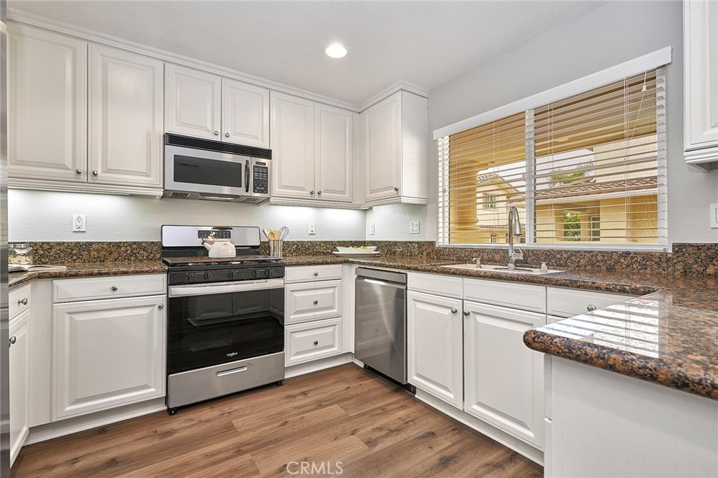 a kitchen with granite countertop white cabinets appliances a sink and a window