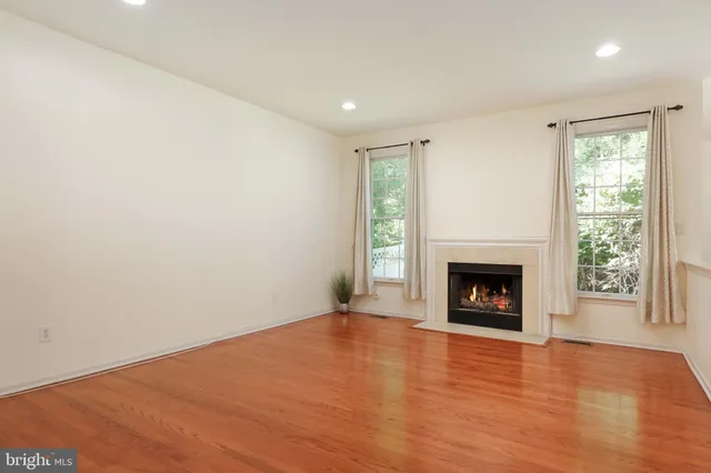 a view of an empty room with wooden floor fireplace and a window