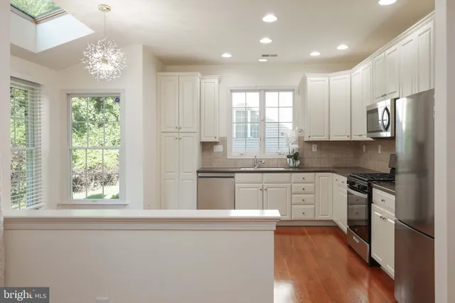 a kitchen with stainless steel appliances granite countertop a stove a sink a refrigerator and white cabinets with wooden floor