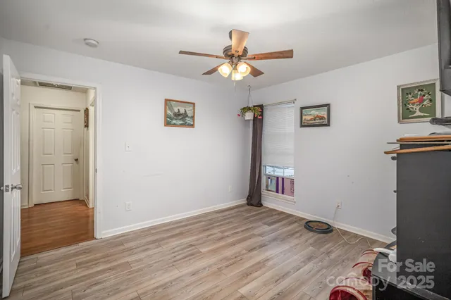a view of an empty room with wooden floor and a ceiling fan