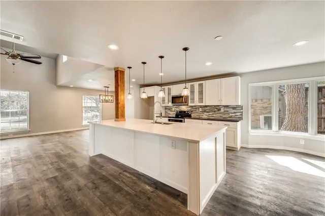 a kitchen with stainless steel appliances kitchen island granite countertop a stove a sink a refrigerator and white cabinets with wooden floor