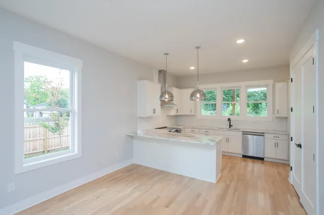 a kitchen with a sink dishwasher a stove and white cabinets with wooden floor