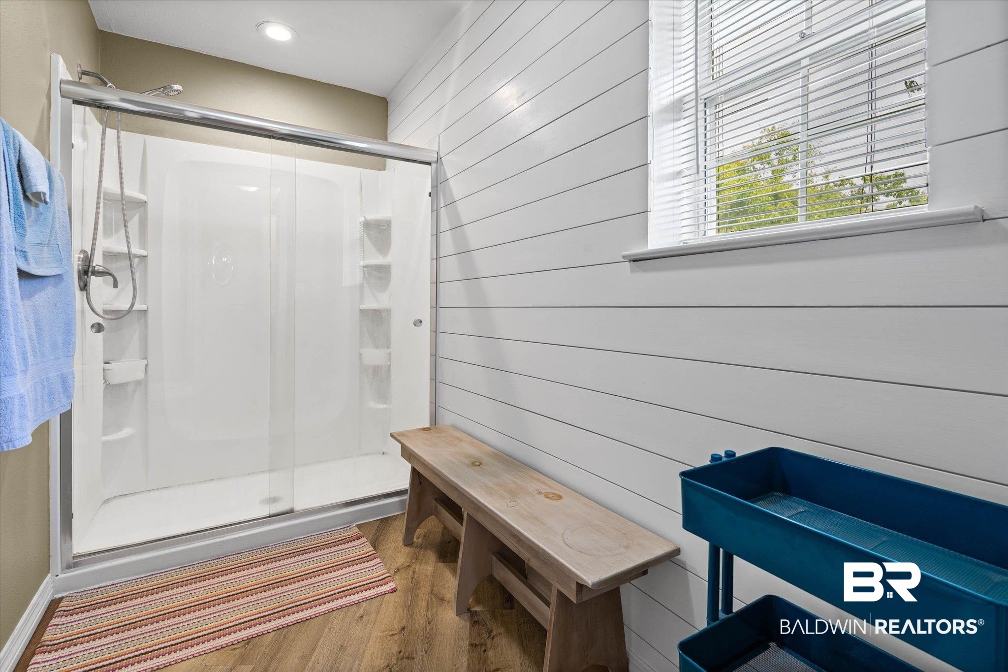 9100 Shell Belt Road Coden, AL 36523 - Photo 17 of 38 Shower enclosure with sliding glass doors, white shiplap wall paneling, wood-finish flooring, and a window with blinds