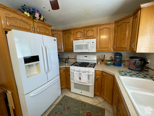 11473 South Dempsey Creek Road Lava Hot Springs, ID 83246 - Photo 9 of 47 Kitchen with white appliances, brown cabinets, light countertops, light tile patterned flooring, and ceiling fan