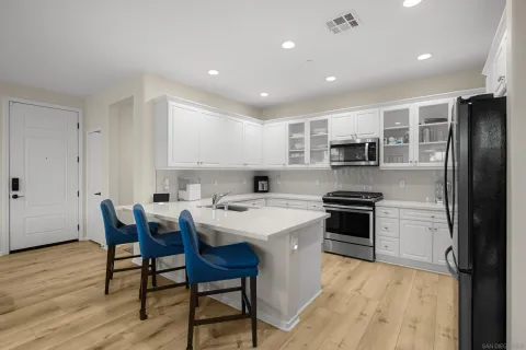 a kitchen with stainless steel appliances a stove a sink a microwave a refrigerator white cabinets and wooden floor